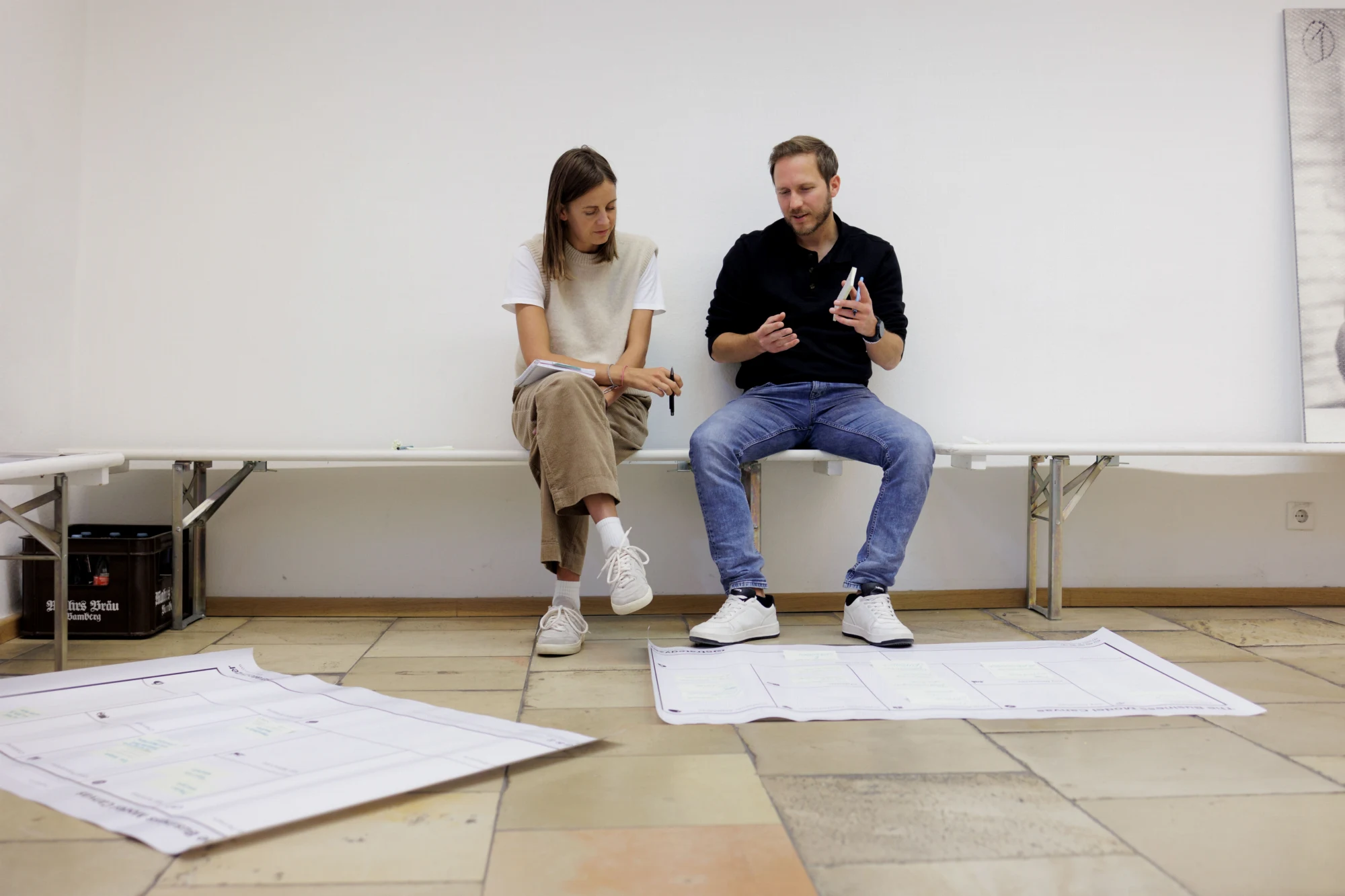 Zwei StärkenCoachs im Gespräch auf einer Bank, vor ihnen Canvas-Bögen